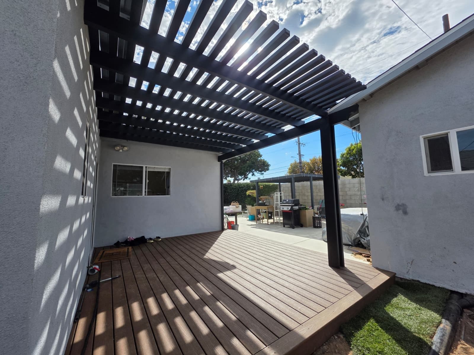 Black slatted pergola casting striped shade over a deck beside a house