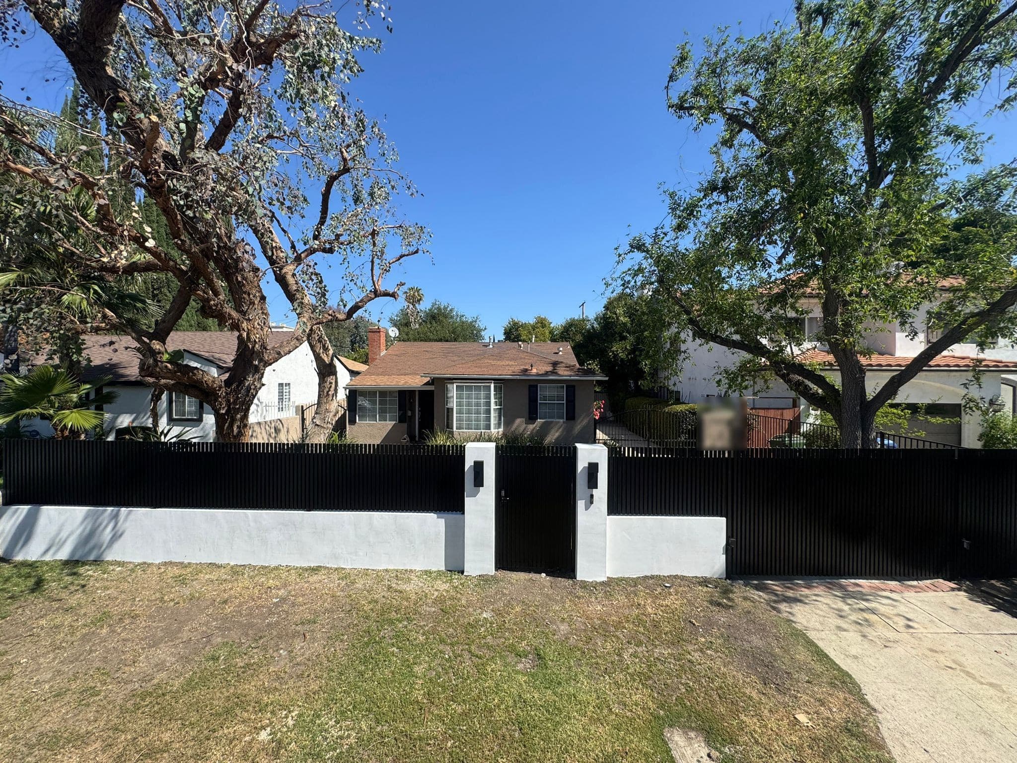 Black vertical-slat fence on a white stucco base with capped, lit pillars and a walk gate