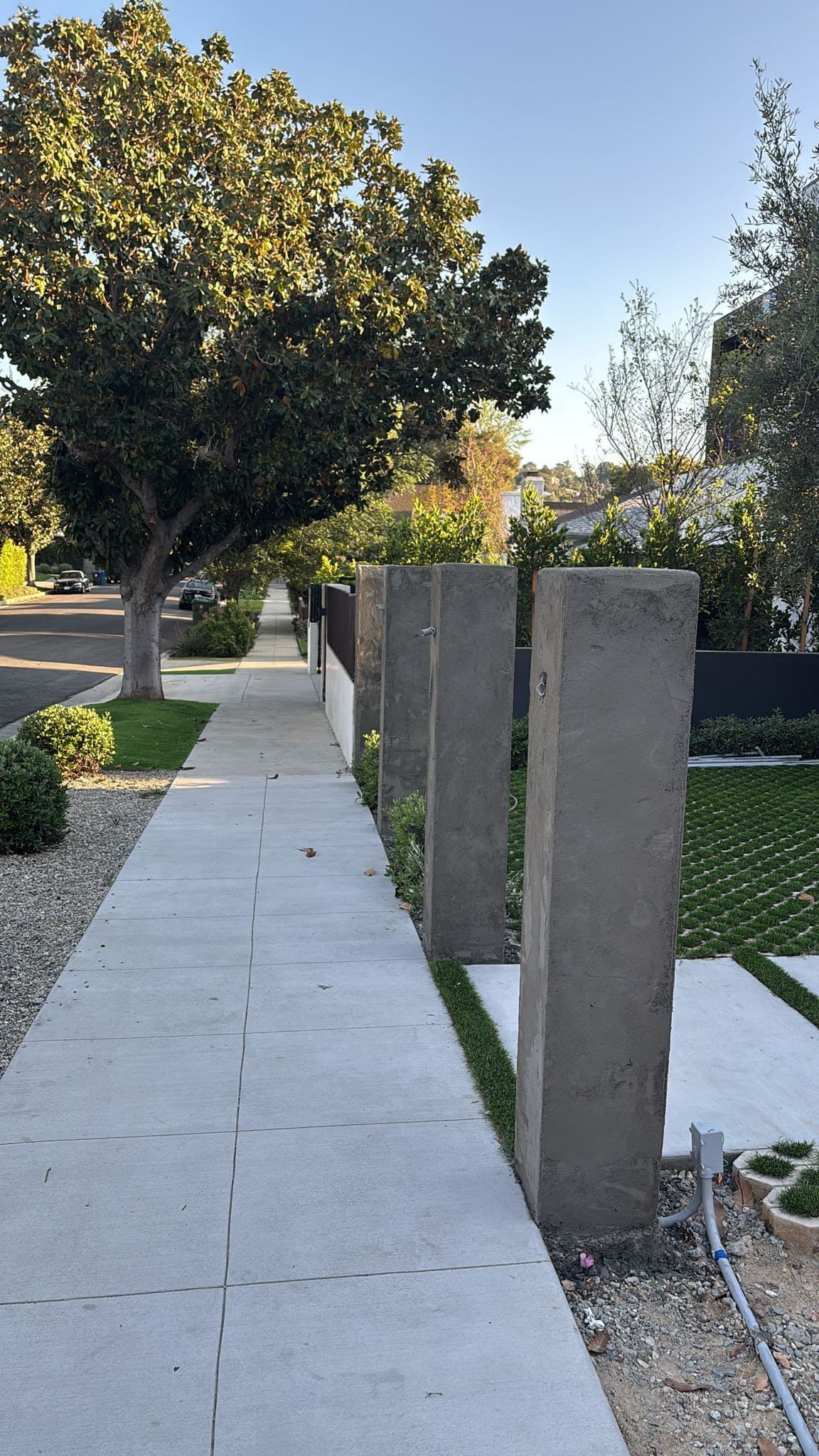 Tall square pillars rising along a new concrete walk in late-day light