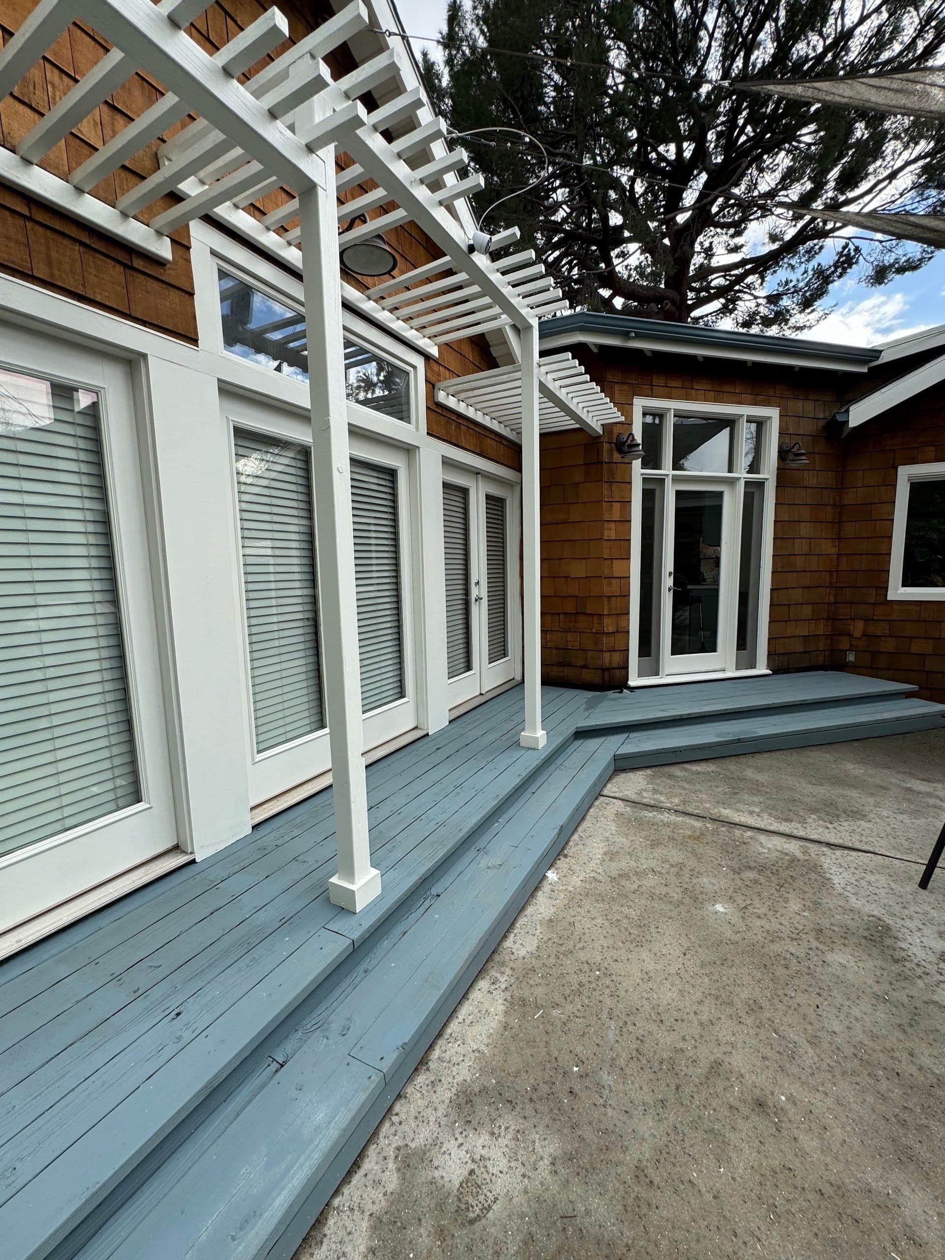 Gray-blue painted deck under a white pergola at the back of a cedar-shingle house