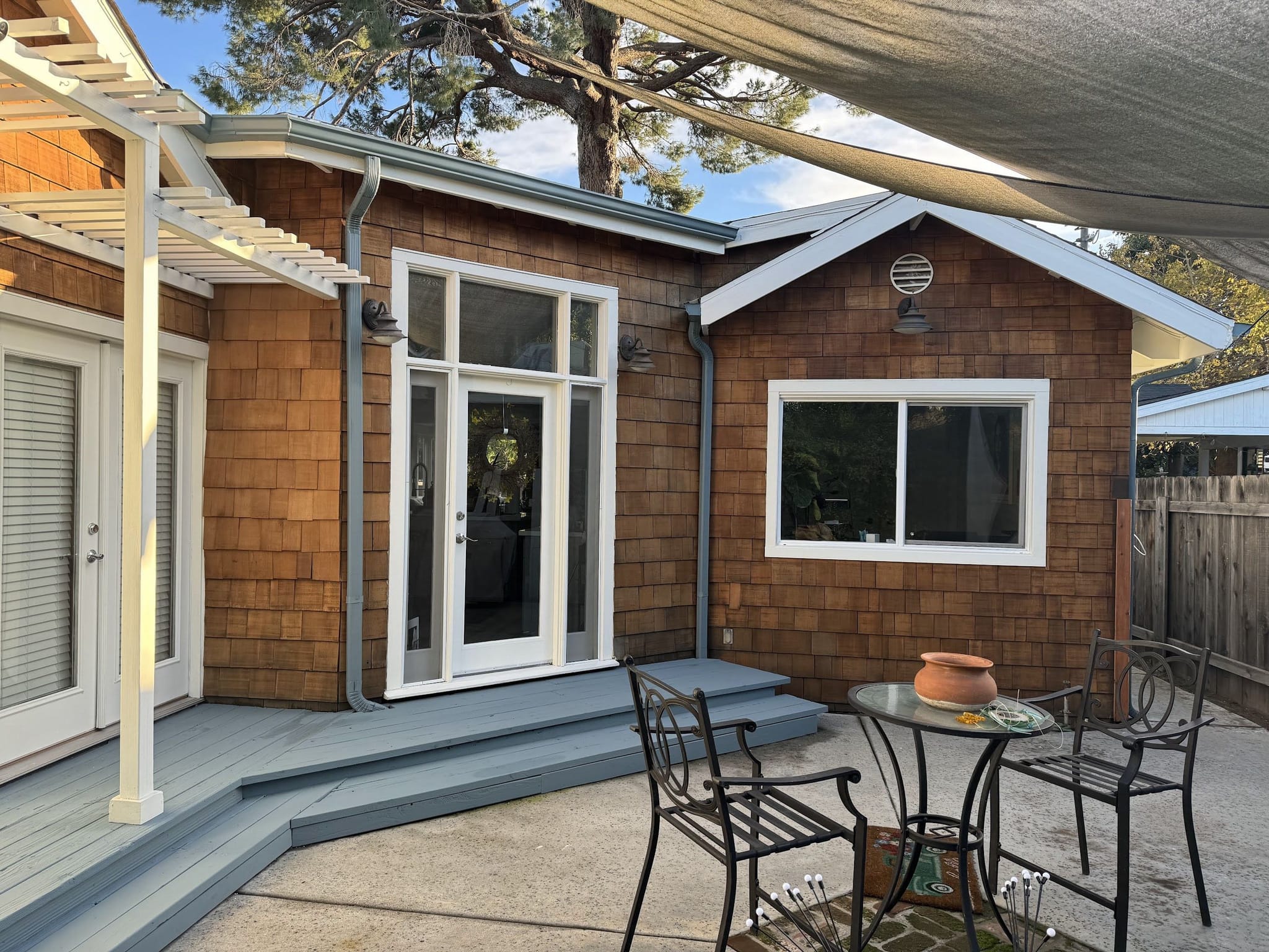 Painted deck and patio behind a cedar-shingle house, a white pergola at the corner