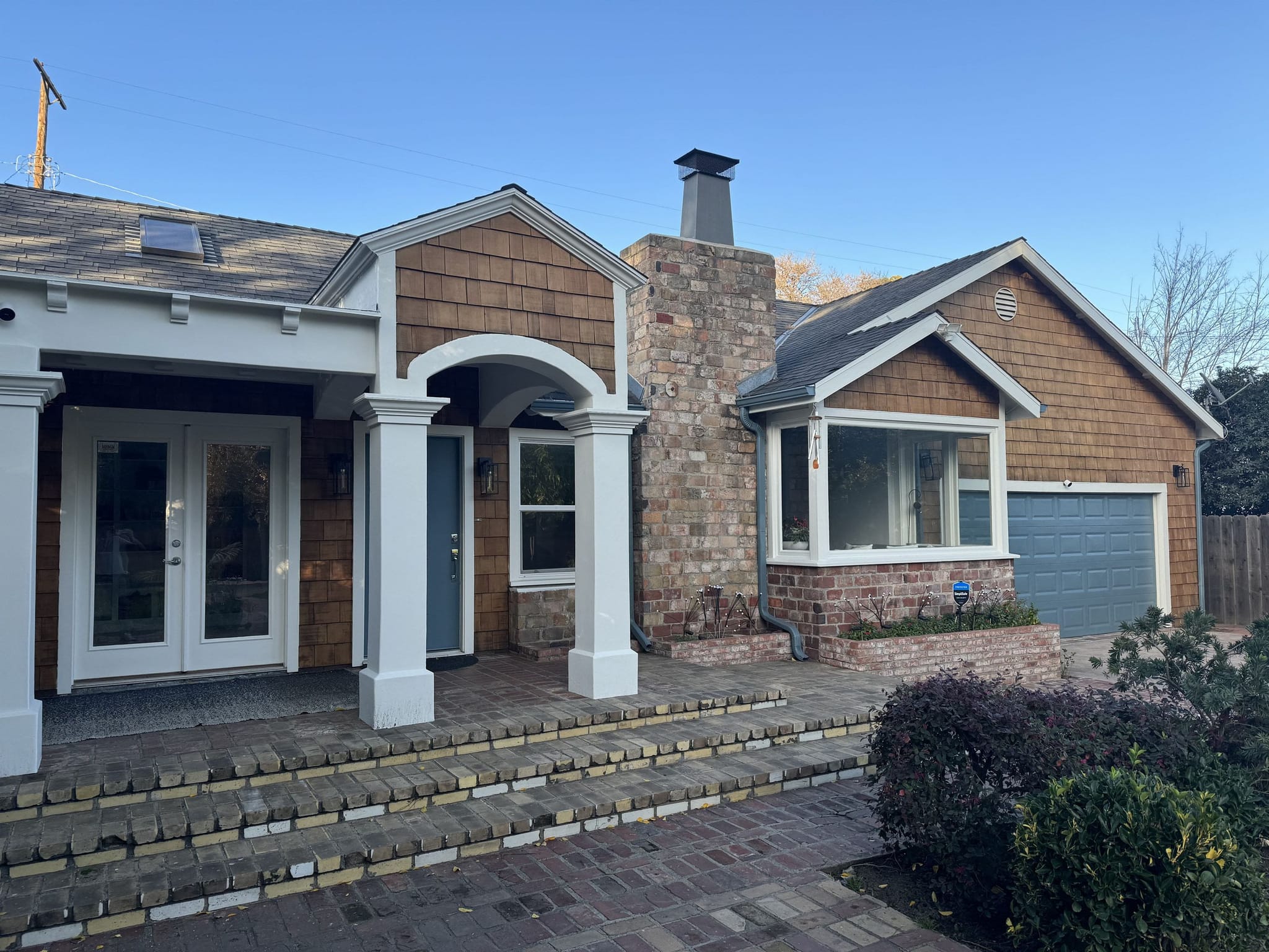 Repainted cedar-shingle house with a white arched portico, brick chimney and a blue garage door