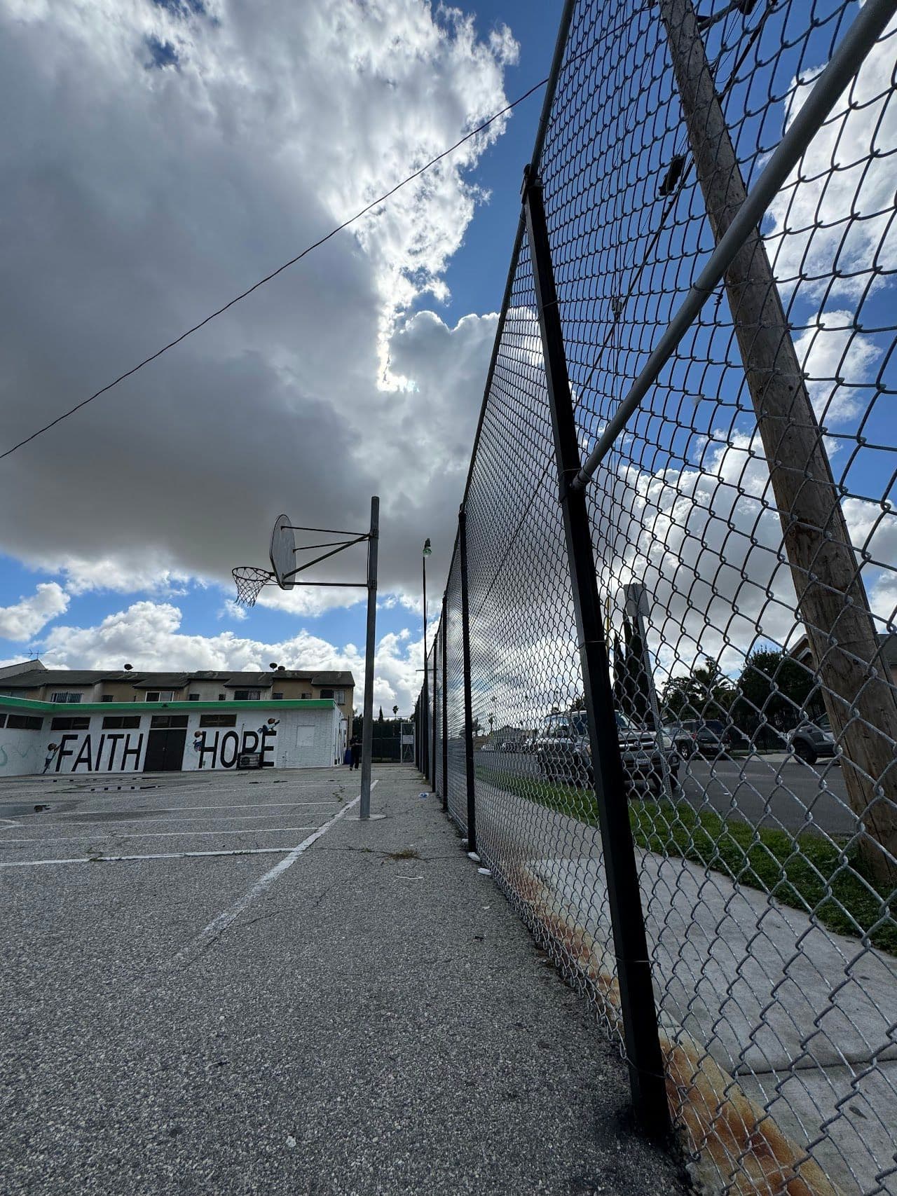 Tall galvanized chain-link fence running along a paved yard under a cloudy sky