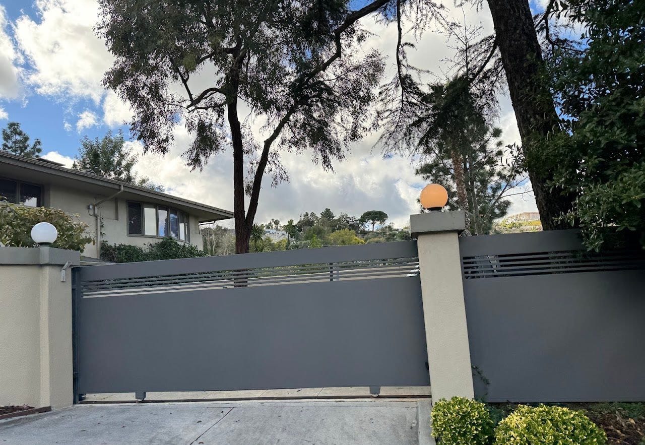 Gray sliding driveway gate between stucco pillars with a matching fence