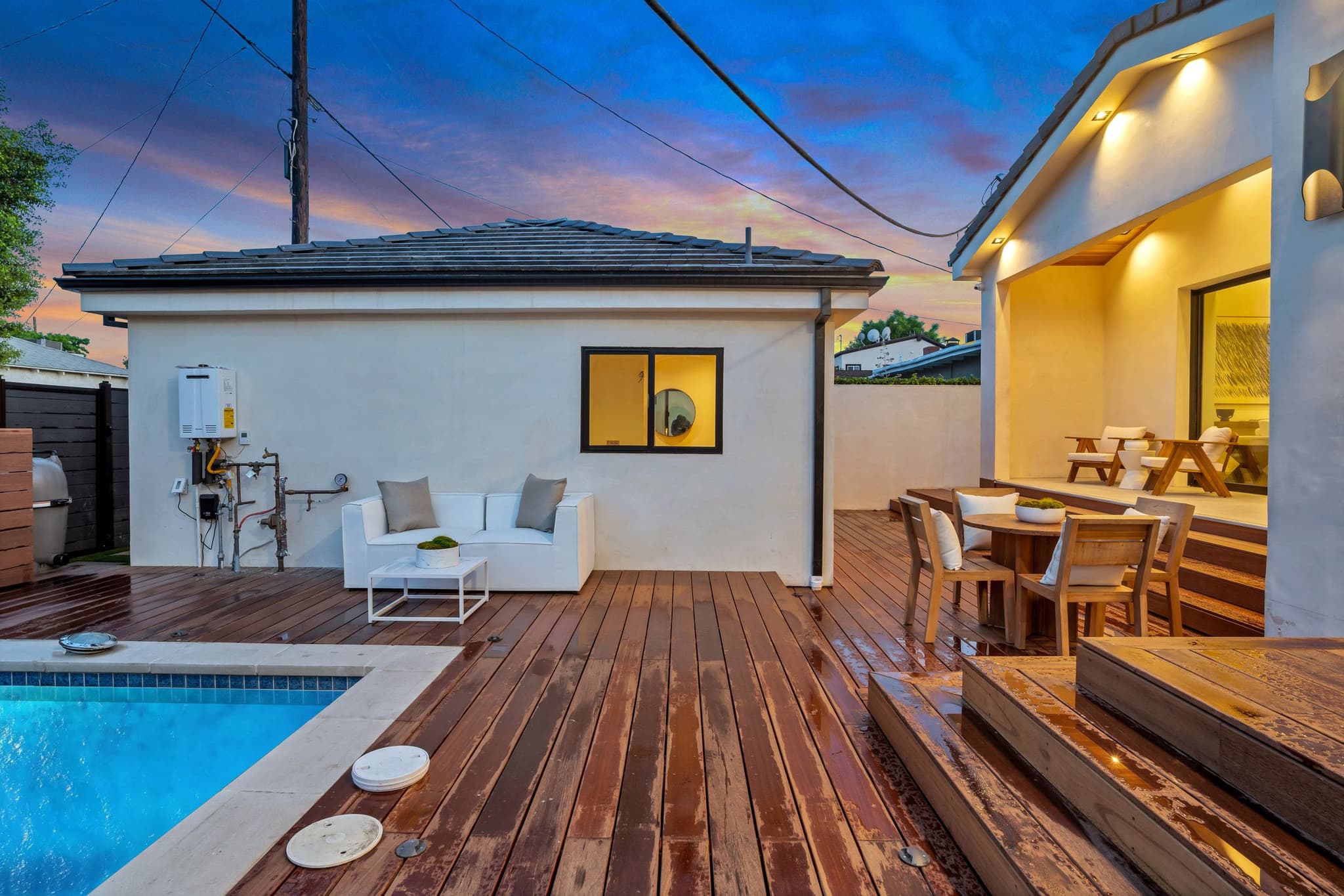 Hardwood deck at dusk running back to a detached stucco building, the pool in front