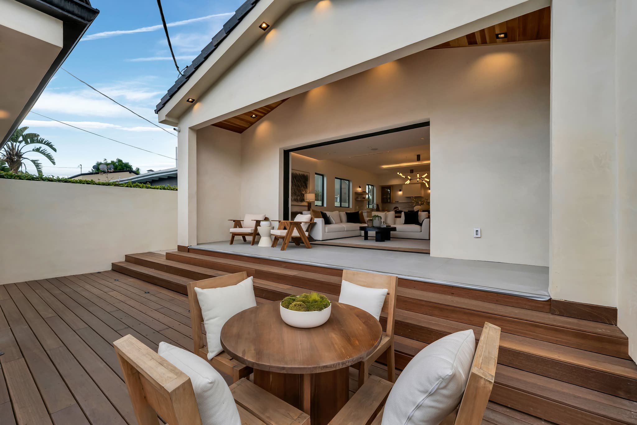 Hardwood deck with wide steps at the back of a new home, glass doors open at dusk