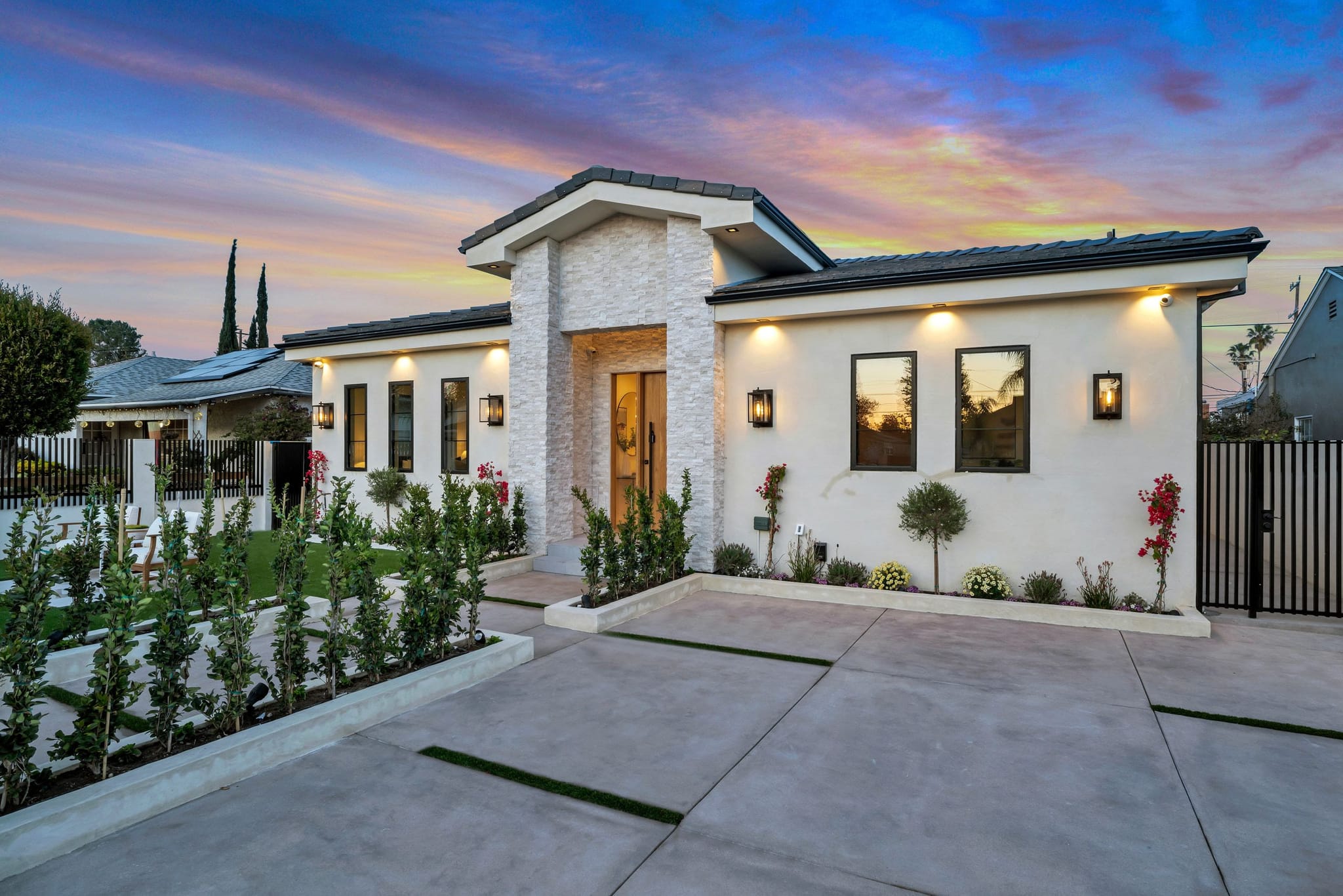 Single-story new home at dusk, white stone entry, warm wall lights and a new front walk