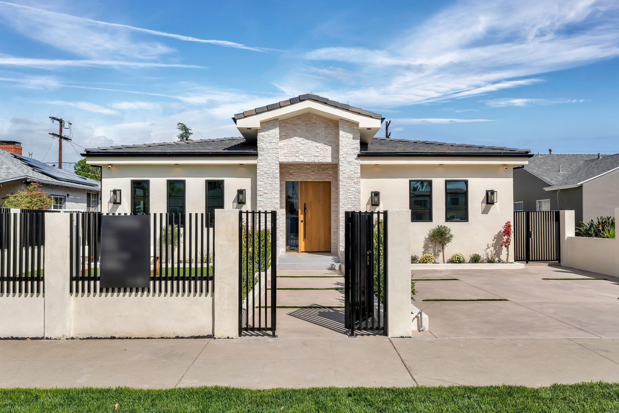 Black metal fence with open double gates leading to the entry of a new home