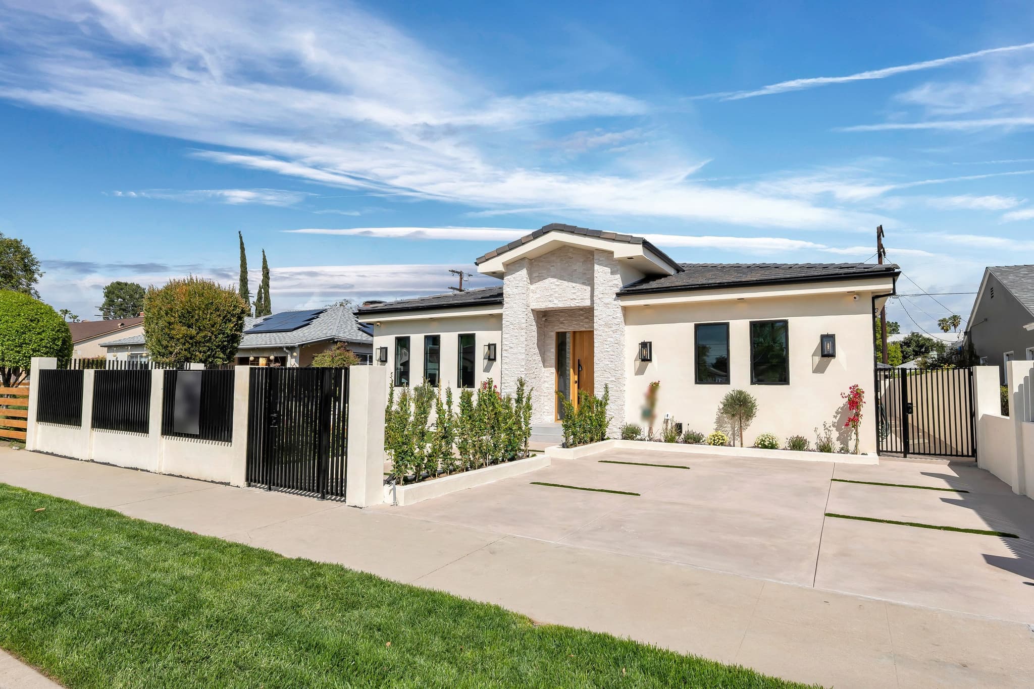 New single-story home behind a black slat fence on a stucco base, with a walk gate and a wide concrete driveway