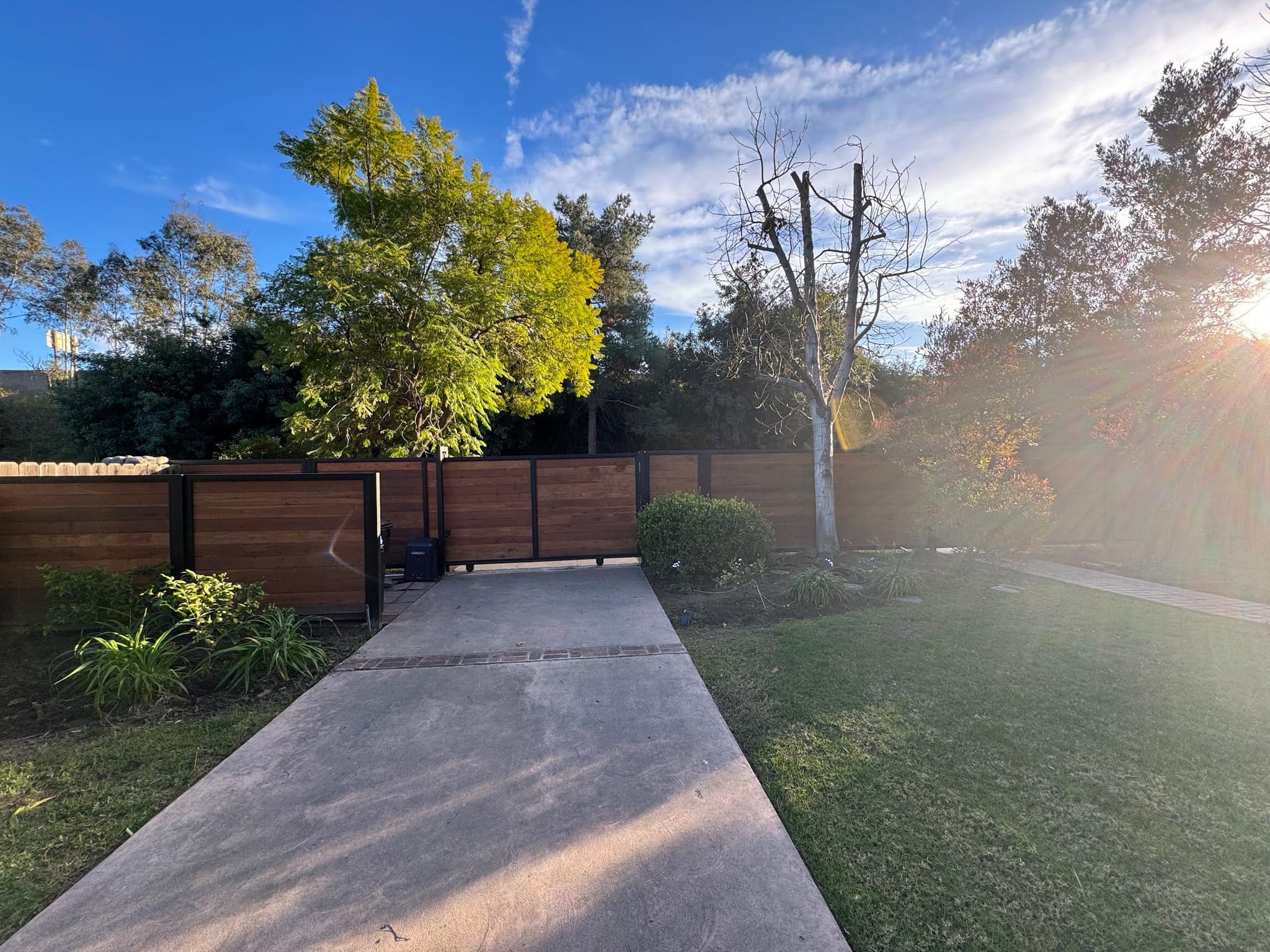 Horizontal redwood fence at the end of a long concrete driveway in low sun