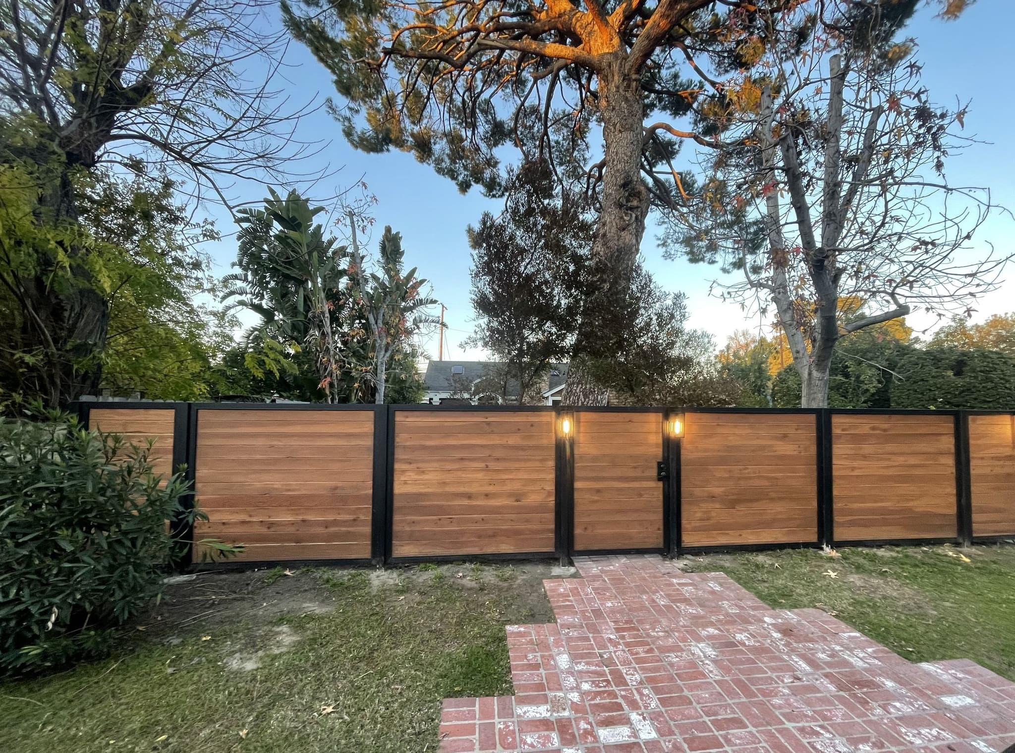 Horizontal redwood fence with black steel posts and lanterns along a brick walk