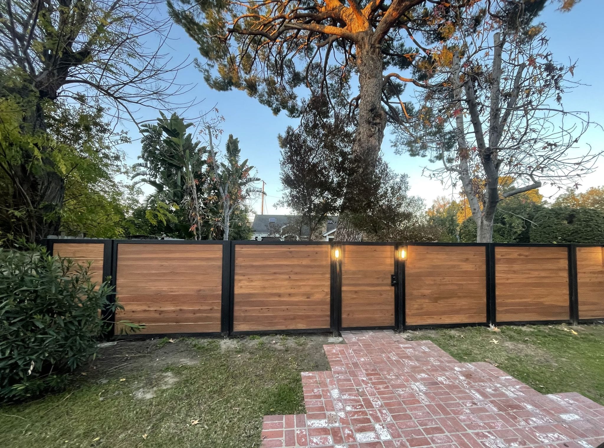 Horizontal redwood fence with black steel posts and lanterns along a brick walk