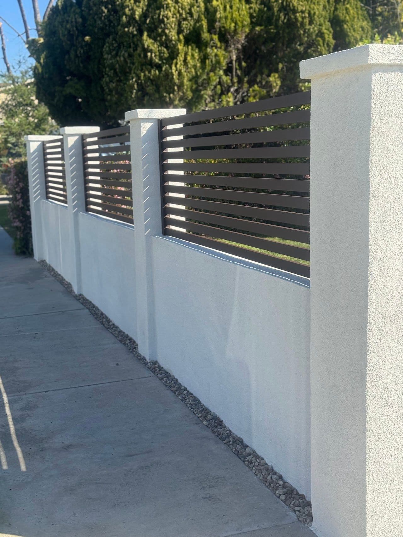 Stucco wall with pillars and horizontal slat infill along a sidewalk
