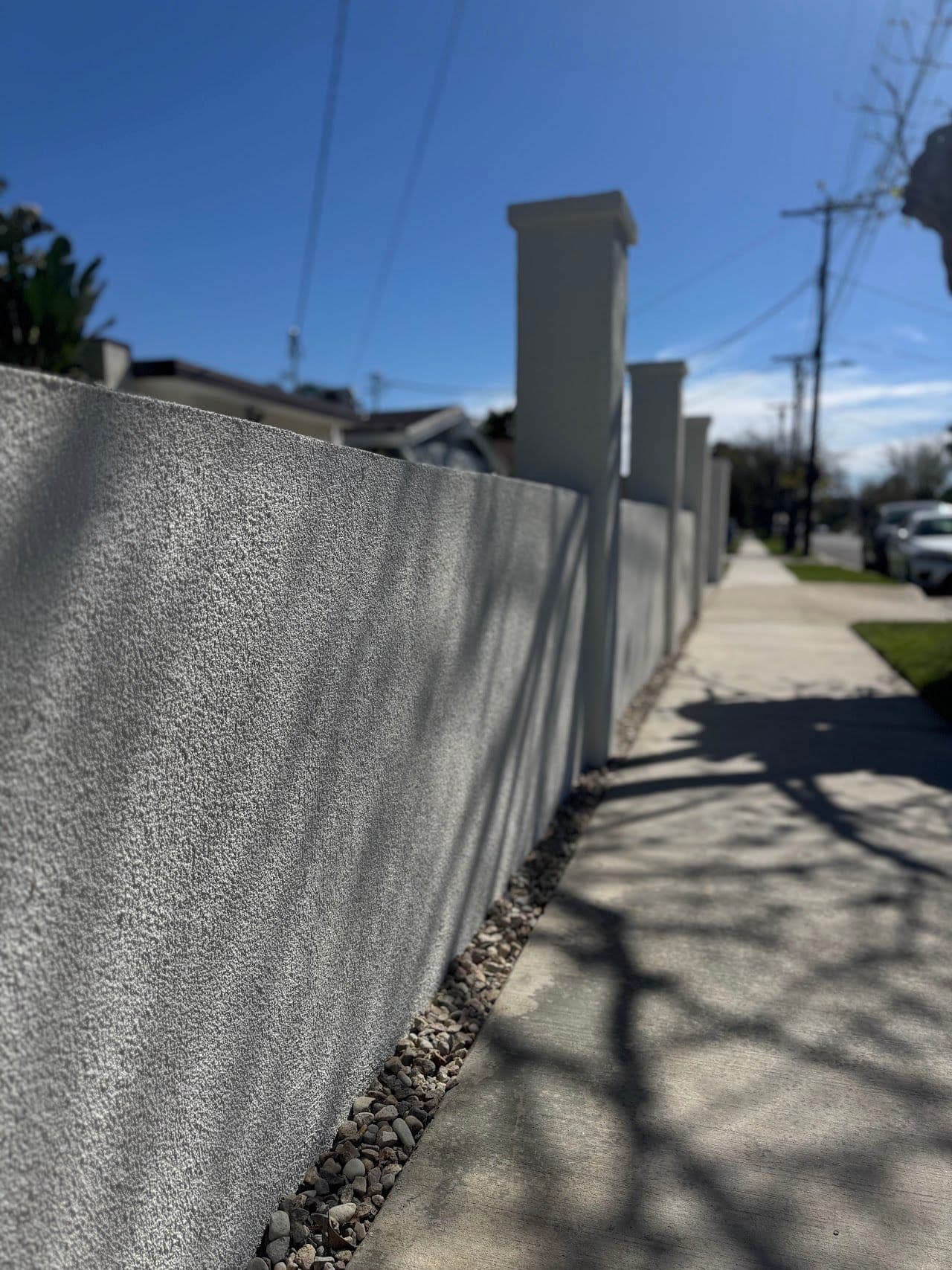 Long smooth stucco wall with capped pillars along a sidewalk