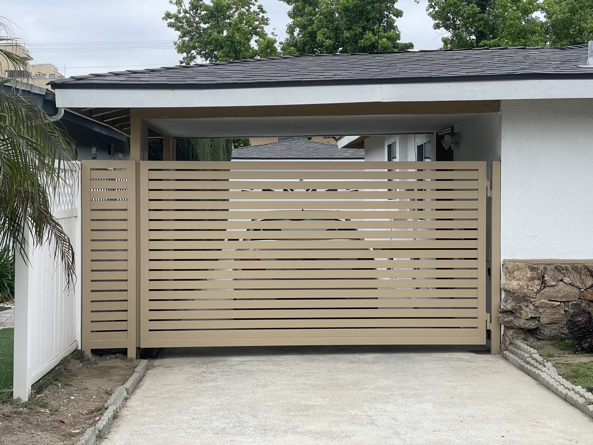 Tan horizontal-slat metal swing gate closing off a carport
