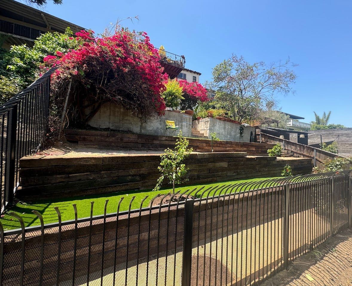 Terraced backyard with retaining walls, turf and a black metal fence