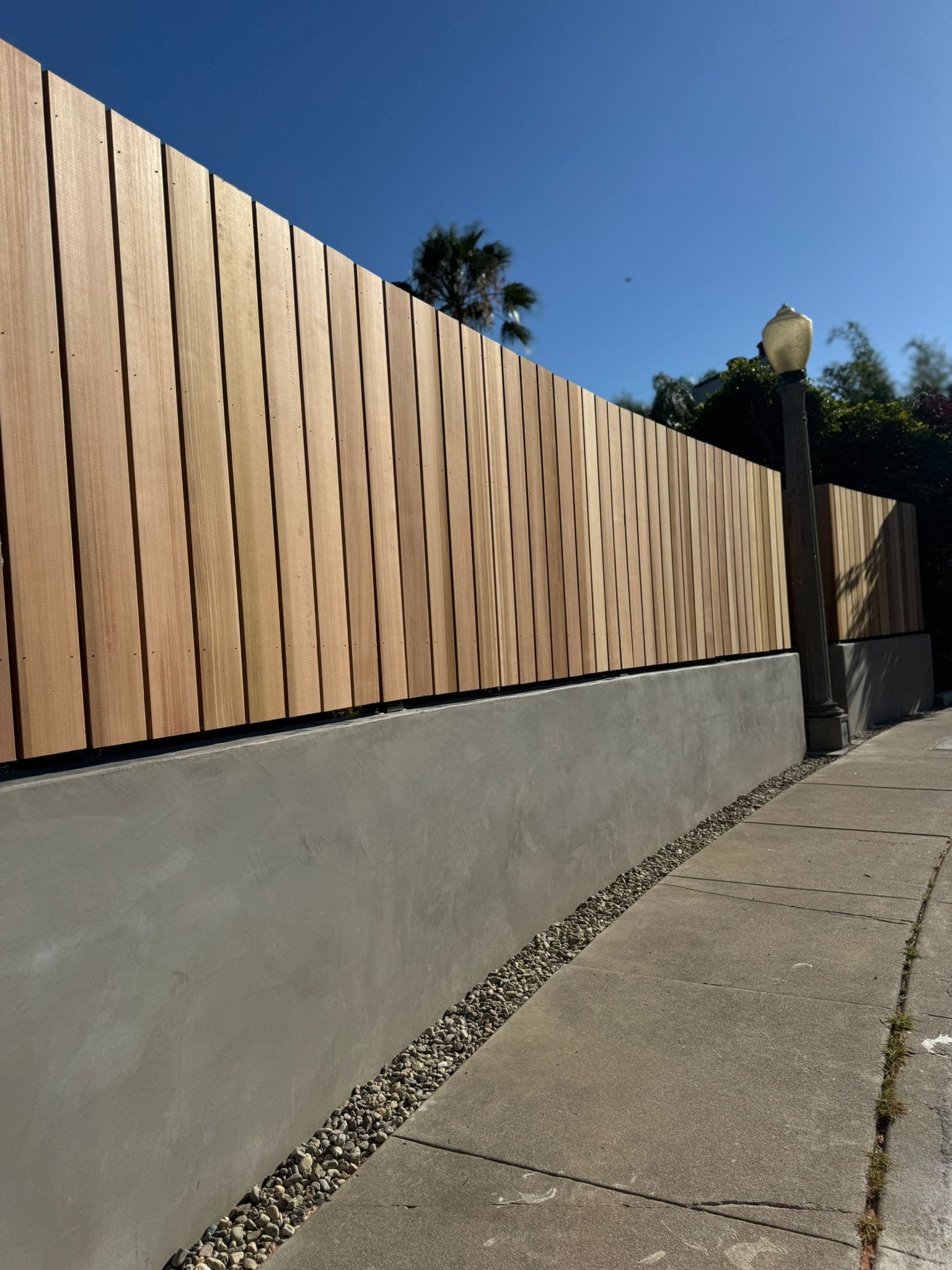 Vertical wood fence boards on a gray stucco base running along a sidewalk