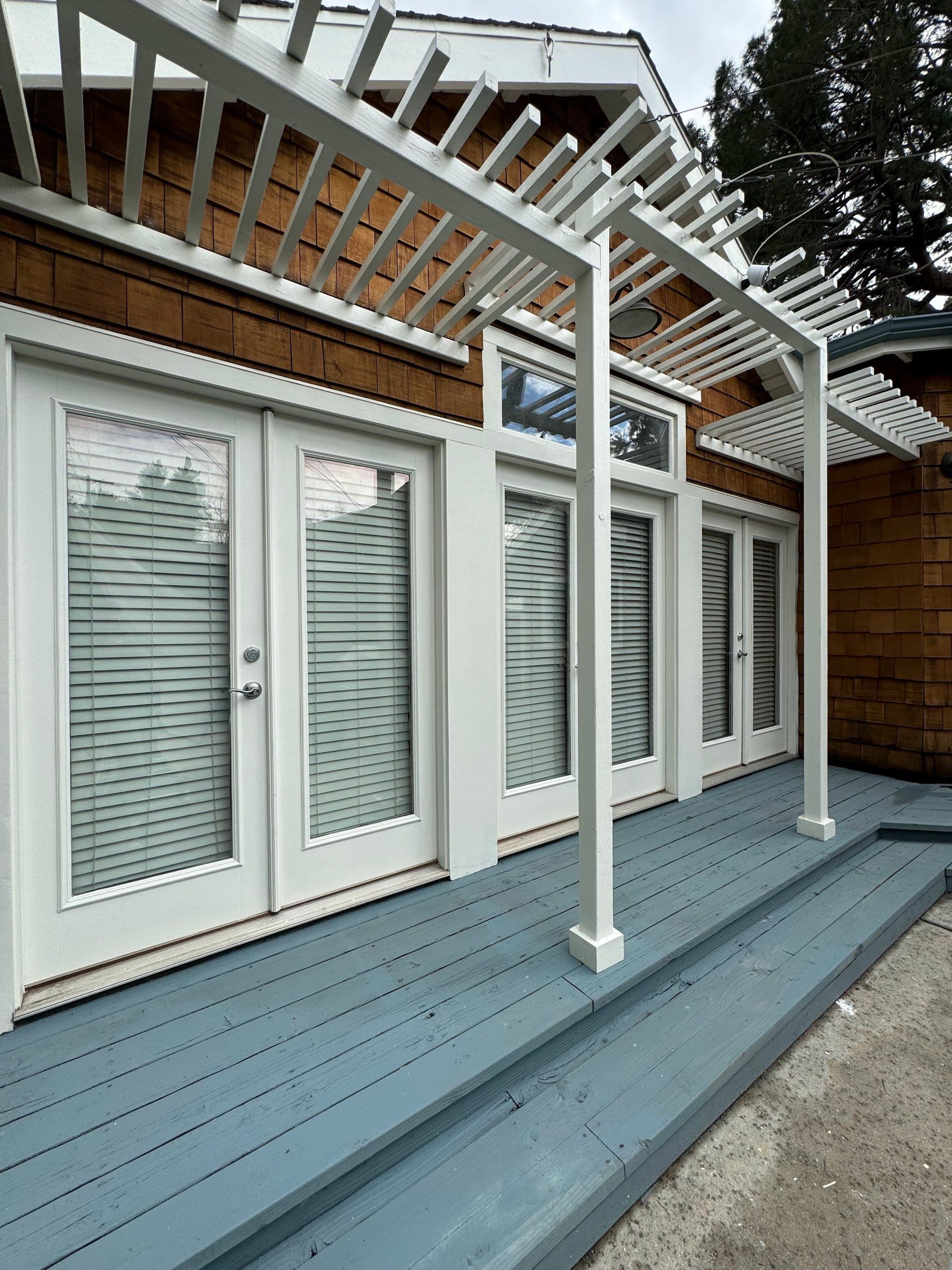 White pergola over a painted deck and French doors