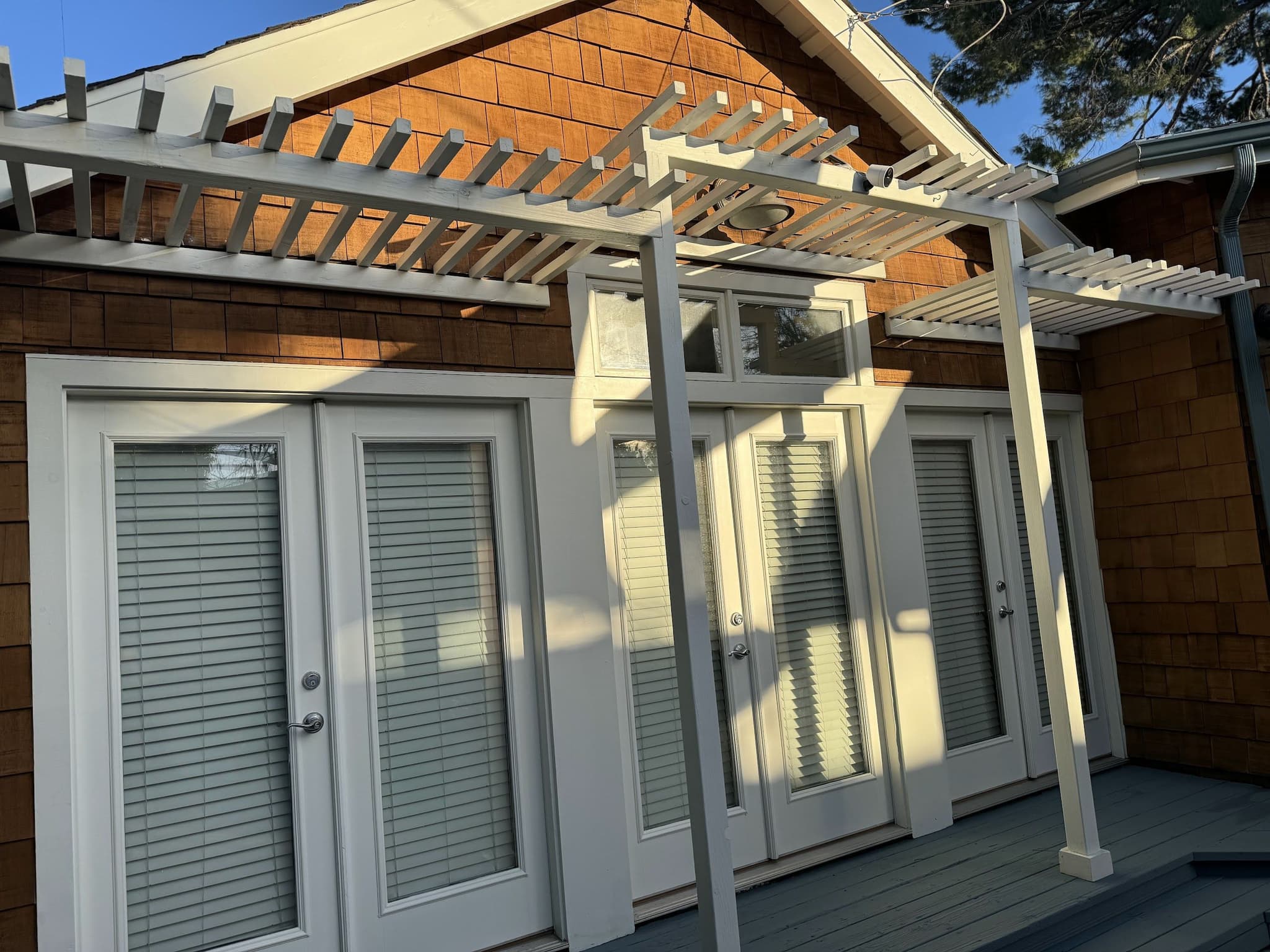 White pergola over French doors on a cedar-shingle house