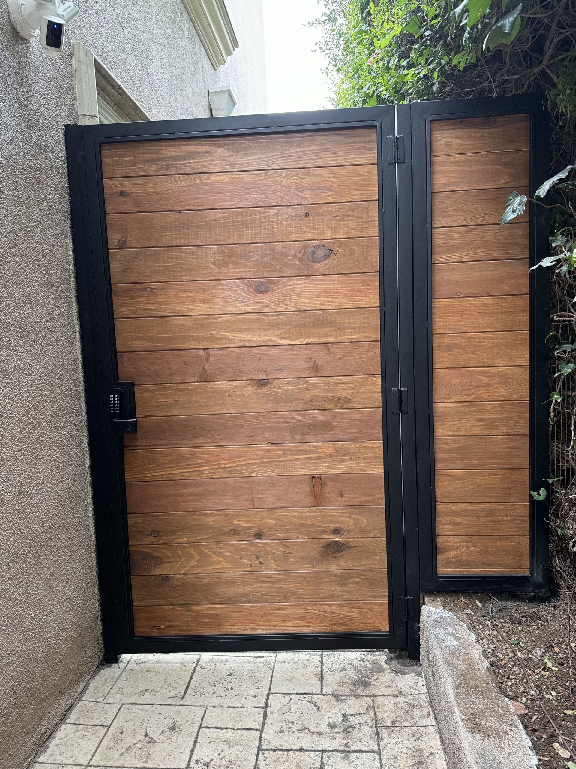 Wood walk gate with horizontal boards in a black steel frame, closing a narrow side yard